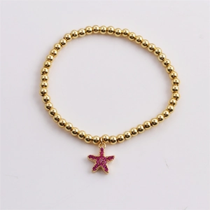 Détail d'un bracelet à billes dorées avec un pendentif étoile de mer en zircon rose