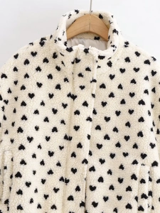 Nahaufnahme der weißen Fleecejacke mit schwarzen Herz-Prints und weicher Textur auf Holzbügel