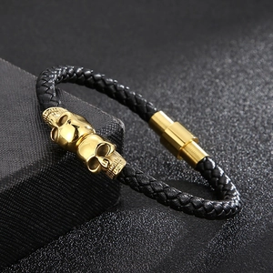 Detail of black braided leather bracelet featuring golden skull charms and magnetic clasp