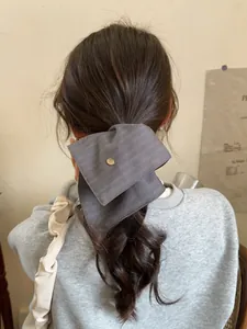 Detail of grey-purple textured fabric bow hair accessory with a gold metal center button