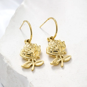 Detailed macro view of 18k gold plated rose shaped earrings with stem and leaf on stone