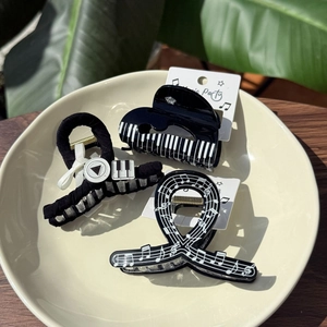 Minimalist piano keyboard and music note hair clips displayed on a tray on wooden background