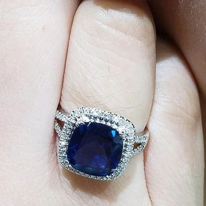 Macro shot of cushion-cut blue sapphire ring with pavé diamonds on silver split shank band