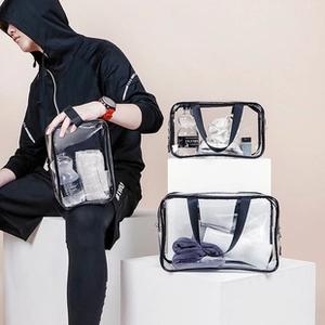Three sizes of transparent PVC toiletry bags with handles shown in a lifestyle studio setting