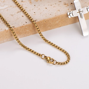 Golden box chain with a silver hollowed cross pendant on a minimalist stone base