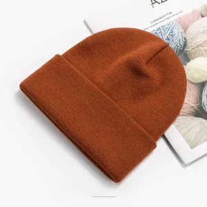 Detail view of a caramel knit beanie on a white surface with minimalist magazine