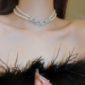 Detail of layered pearl necklace featuring silver diamond-encrusted flower on neck