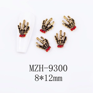 Detailed view of skull hand nail charms with red rhinestones and vintage gold finish