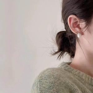 Close-up of small silver textured earrings worn by a model in a light green sweater