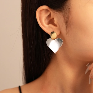 Close-up of model wearing geometric heart earrings with gold and silver color-blocking