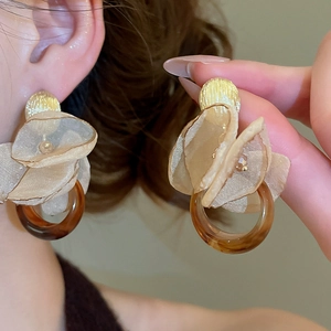 Macro detail of elegant champagne chiffon flower earrings with amber resin ring and gold stud