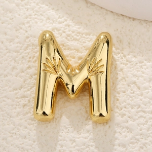 Macro detail of 3D bubble letter M pendant with shiny gold finish and etched textures