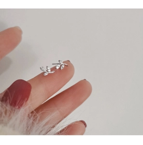 Detail of silver leaf earrings with inlaid crystals held on fingertips for scale