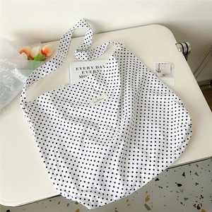 Detail of canvas tote bag showing black polka dots and woven brand label on white surface