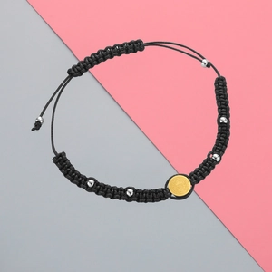 Close-up of black braided cord bracelet with silver beads and golden religious emblem