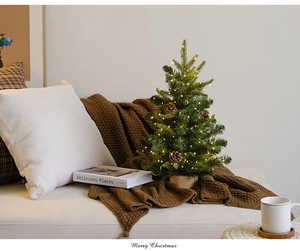 Mini Christmas tree with pine cones and LED lights on cozy sofa setting