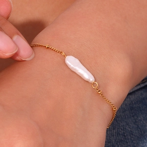 Detail of a gold bracelet featuring a baroque pearl on a woman's wrist with denim