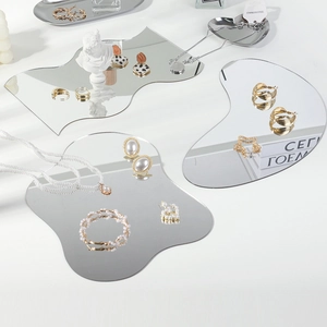Macro shot of irregular acrylic mirror trays displaying jewelry on a white background