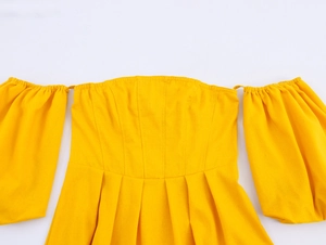 Detail of off-the-shoulder yellow dress featuring pleated waist and puffy sleeves