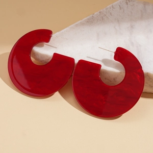 Detailed close-up of C-shaped red marbled acrylic hoops on a stone display pedestal