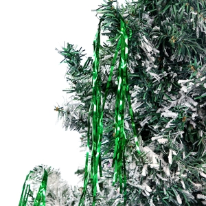 Close-up of green flocked Christmas tree branches with snow effect and foil tinsel