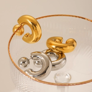 Polished stainless steel C-shaped ball earrings in gold and silver finish on a tray