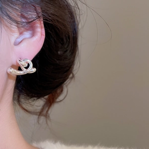 Gros plan de boucles d'oreilles torsadées en métal argenté portées par un mannequin chic