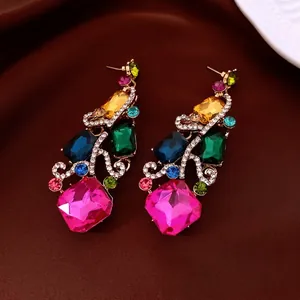 Luxurious gold-tone drop earrings with vibrant multi-color rhinestones on dark velvet