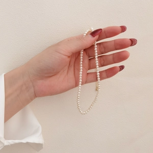 Elegant natural white pearl necklace held by hand, classic single strand jewelry for women