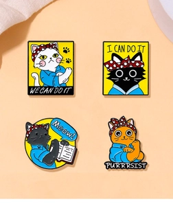 Detail shot of four cat enamel pins featuring motivational slogans and Rosie the Riveter pose
