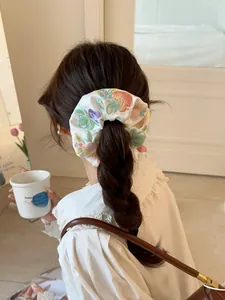 Close-up of white satin scrunchie with floral embroidery worn on a low ponytail hair