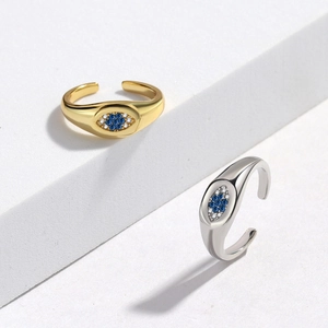 Detail of gold and silver evil eye rings with blue crystals on white geometric stands