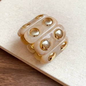 Macro shot of marble resin bracelet with gold studs on a textured beige background