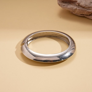 Polished silver metal hinged cuff bracelet with thick dome design on stone background