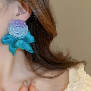 Detailed close-up of large purple resin flower and blue satin bow earring on model