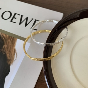 Detailed view of textured gold and silver bangles with irregular hammered finish on a ceramic plate