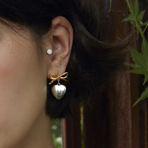 Contrast heart and bow earrings in gold and silver finish worn by a model