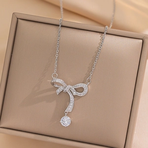 Silver bow necklace with zircon stones on a gold jewelry box, high quality close-up view