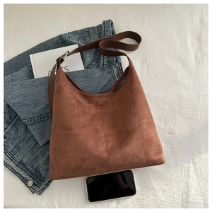 Detailed view of brown matte suede hobo bag on white cloth with accessories