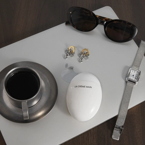 Crème mains ovale chic présentée avec accessoires métalliques et lunettes sur bureau