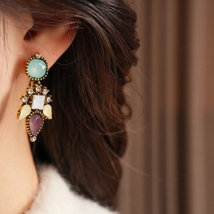 Detail of vintage gold earrings with colorful gemstones worn by model in a soft lighting scene