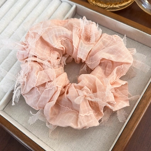 Detail of pink fabric scrunchie with lace mesh edges inside a beige jewelry gift box