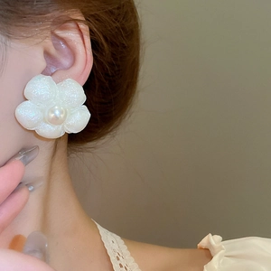 Detailed close-up of a floral earring with a white pearl on a female model