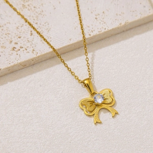 Close-up of golden bow-tie necklace with a sparkling round zircon on stone background