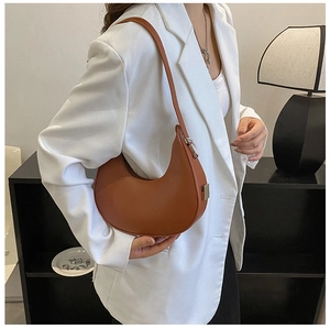 Brown half-moon baguette bag with silver buckle worn by a model in a white blazer