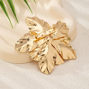 Elegant gold metal maple leaf brooch for women on a decorative tray with natural accents