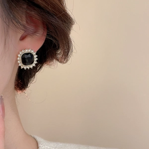 Close-up of elegant gold sunburst stud earrings with black gemstone and white crystals