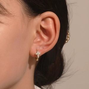 Golden huggie hoop earring with sparkling zircon cross charm worn by a model