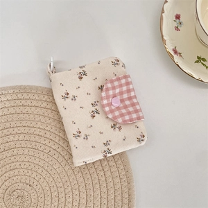 Close-up of floral canvas wallet with pink plaid flap and button on a woven texture mat
