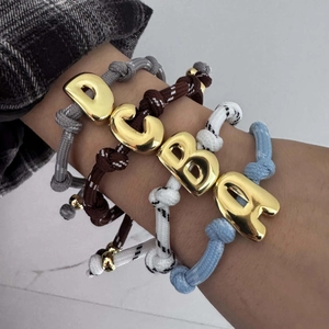 Detailansicht von vier bunten geflochtenen Armbändern mit großen goldenen Buchstabenanhängern.
